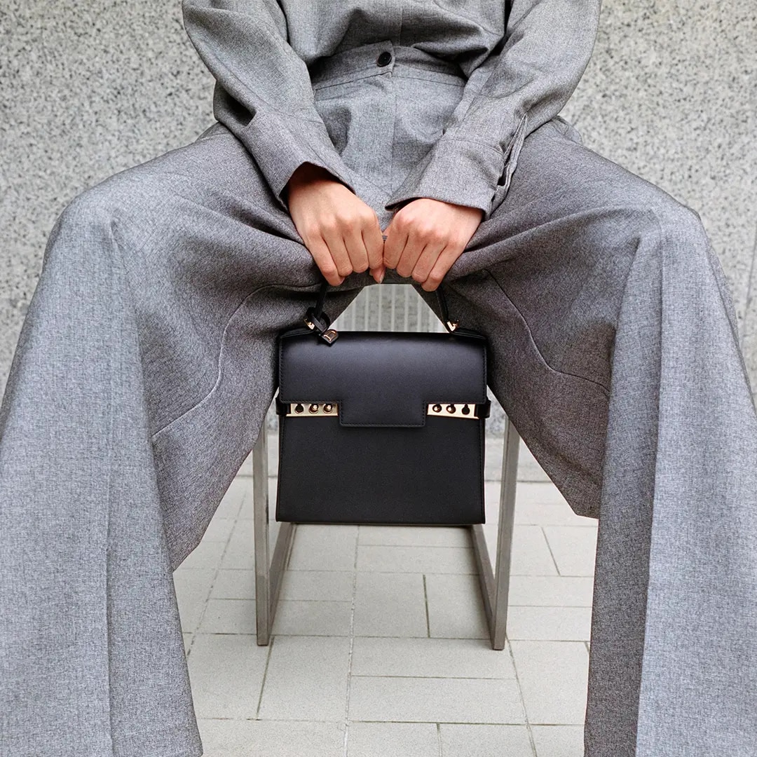 Seating model wearing a grey formal jacket and pant with a Delvaux black bag