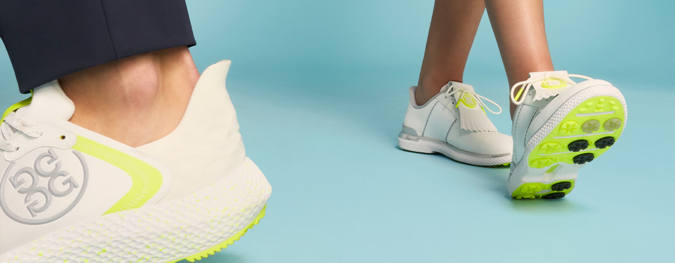 Image showing two people wearing white golf shoes with neon green accents on a light blue surface. The shoes feature a textured sole and the "G/FORE" logo.