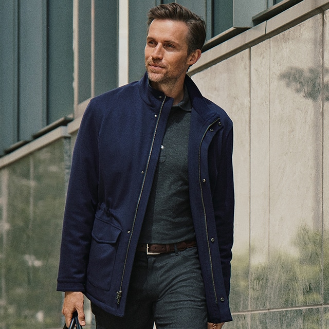 Man Model wearing a blue jacket and a green polo, a brown belt and a grey trouser